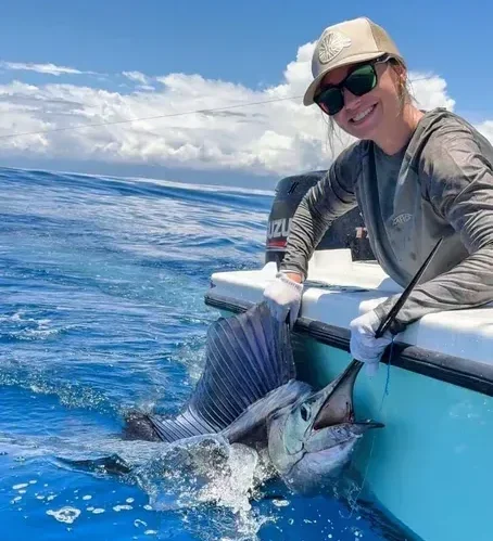 Woman holding a blue marlin in the water beside her boat during an exciting Costa Rica marlin fishing adventure.